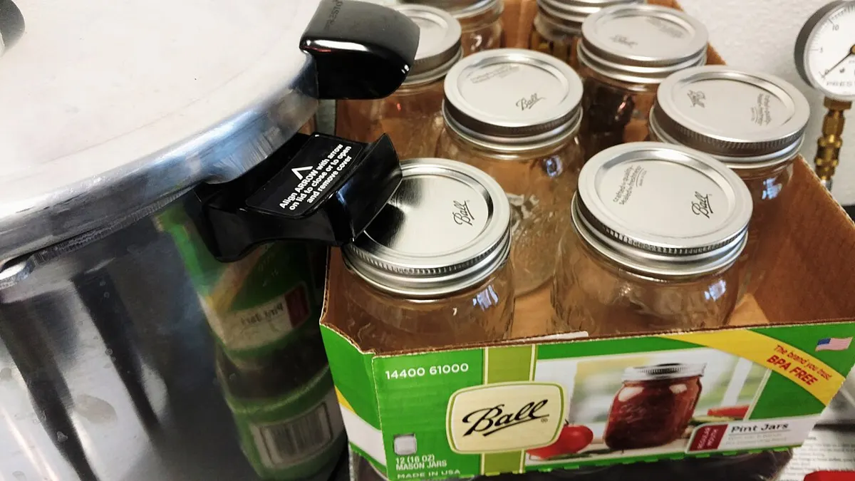 A stovetop pressure canner next to a case of filled pint canning jars